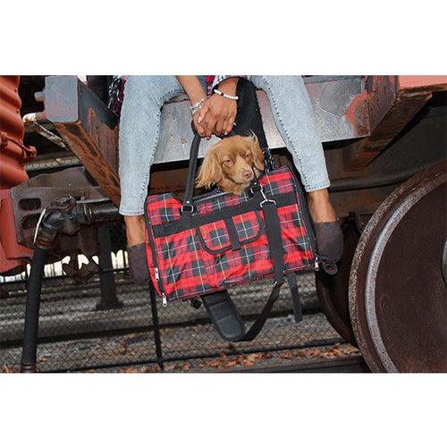 Person holding a red plaid bag with a dog peeking out, standing on train tracks.
