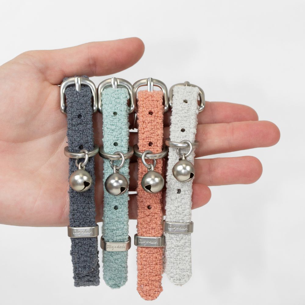 Four cat collars in different colors held in a hand against a white background