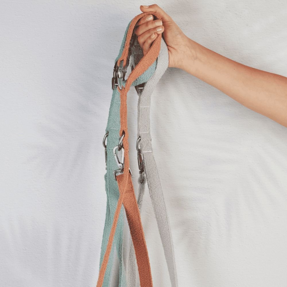 Close-up of a hand holding a striped fabric strap with metal hardware against a light background