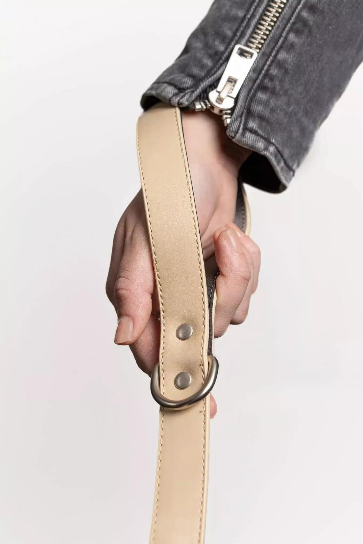 Hand holding a beige leather belt against a light gray background