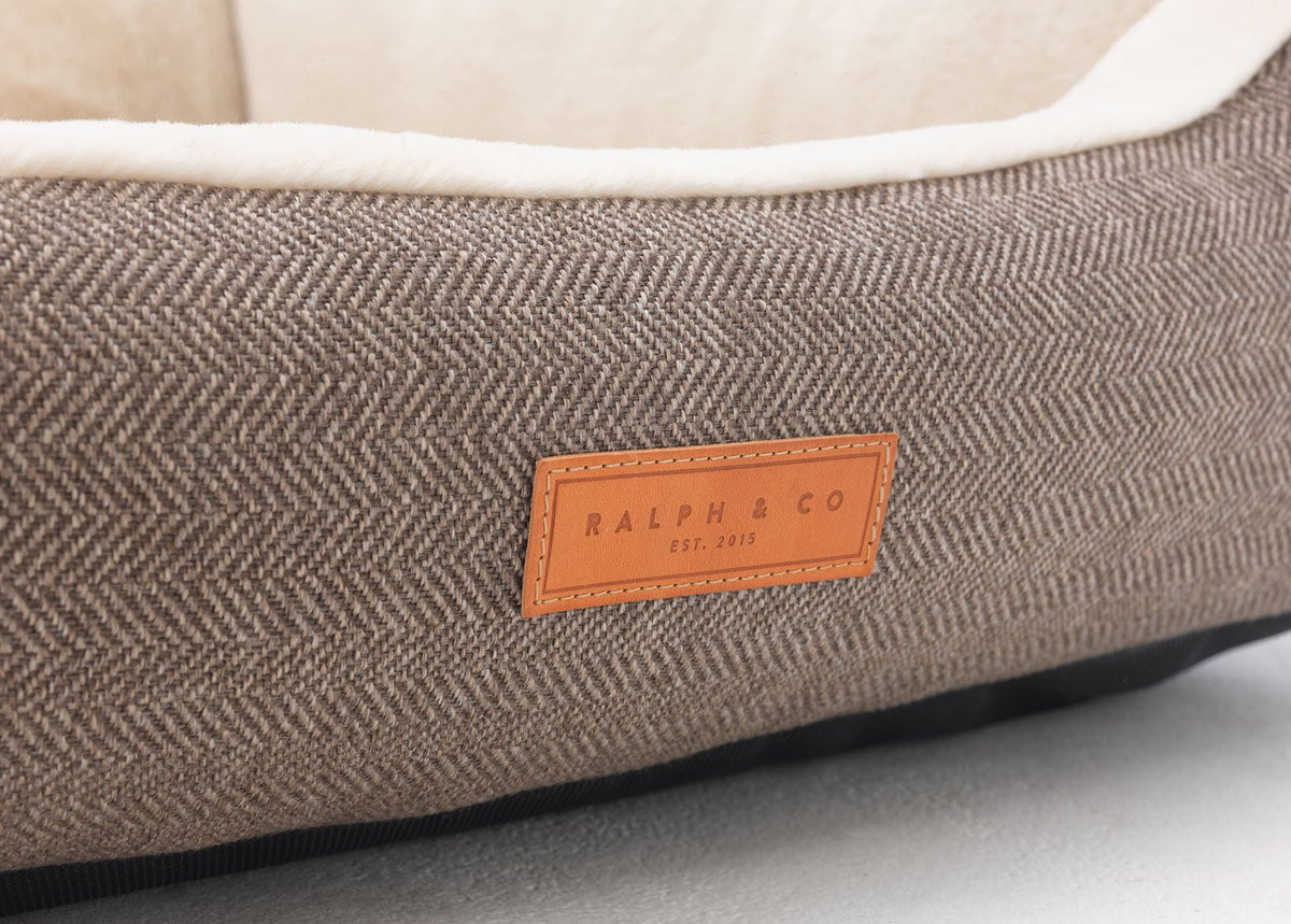 Brown textured pet bed with a leather label on a light gray background