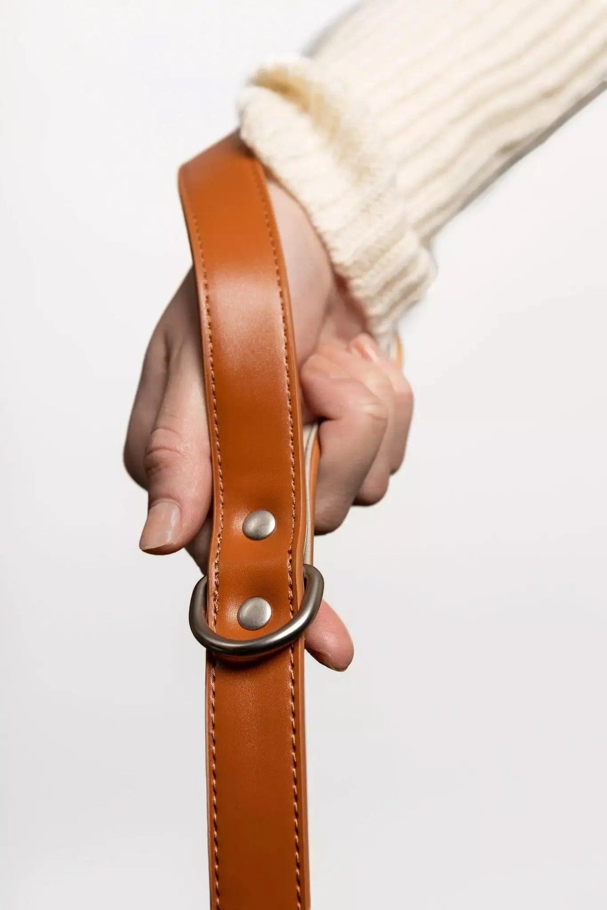 Hand holding a brown leather strap with a metal buckle against a white background