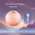 Round pink device with cherry blossom powder and USB cable on a space-themed background