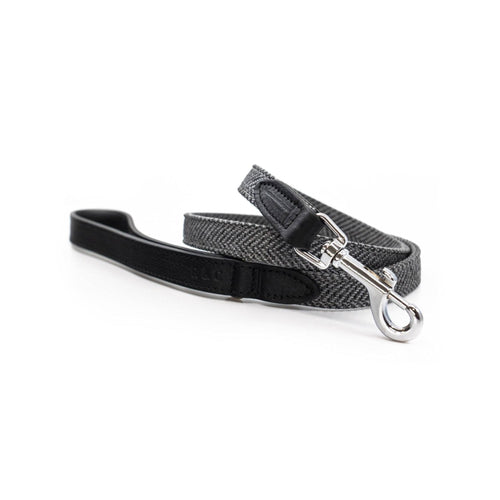 A black and gray herringbone patterned dog leash with a black leather handle and silver metal snap hook, displayed on a clean white background.